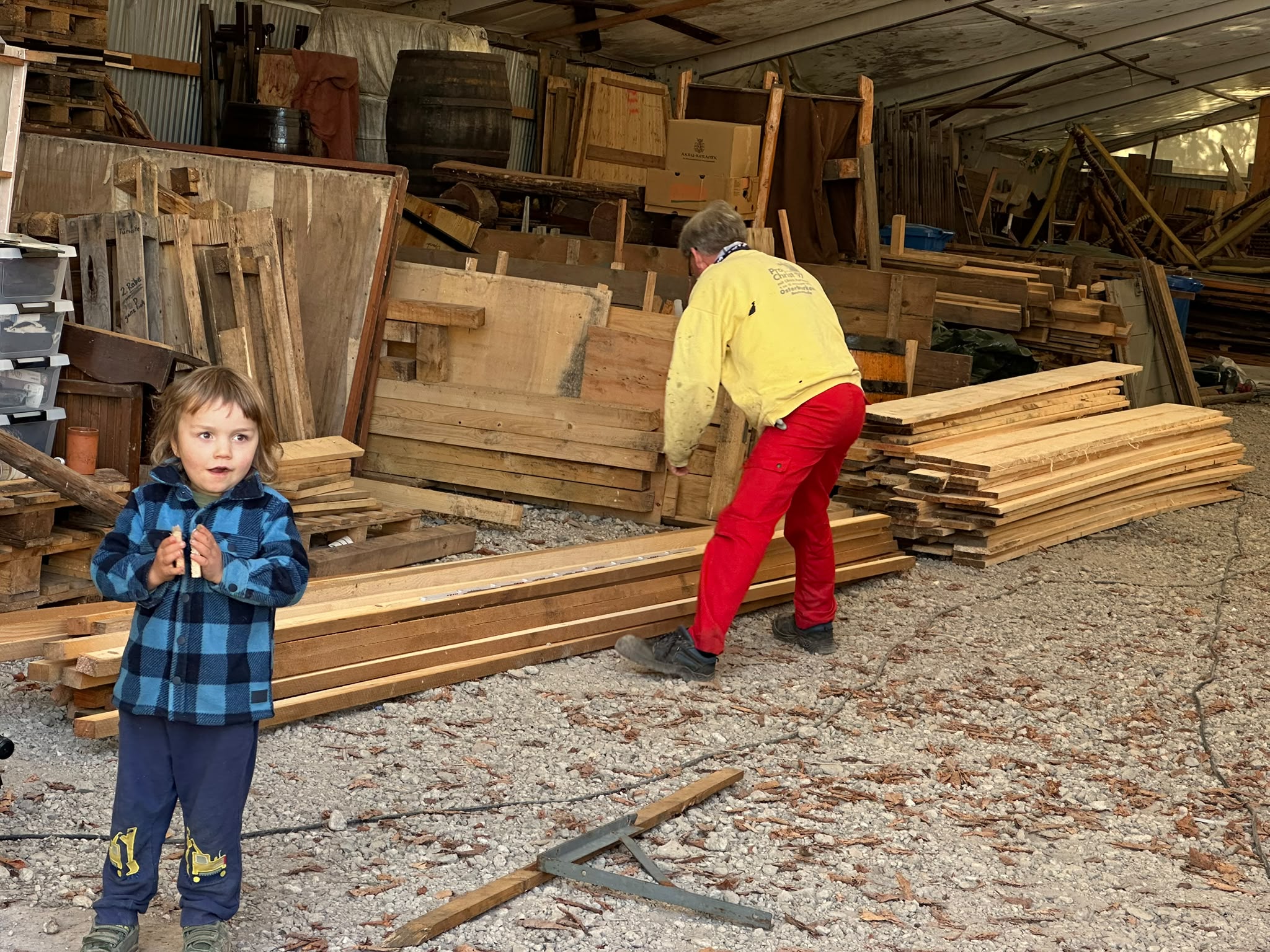 Helfer sortiert Holzbauteile im Lager, ein Kind steht im Vordergrund