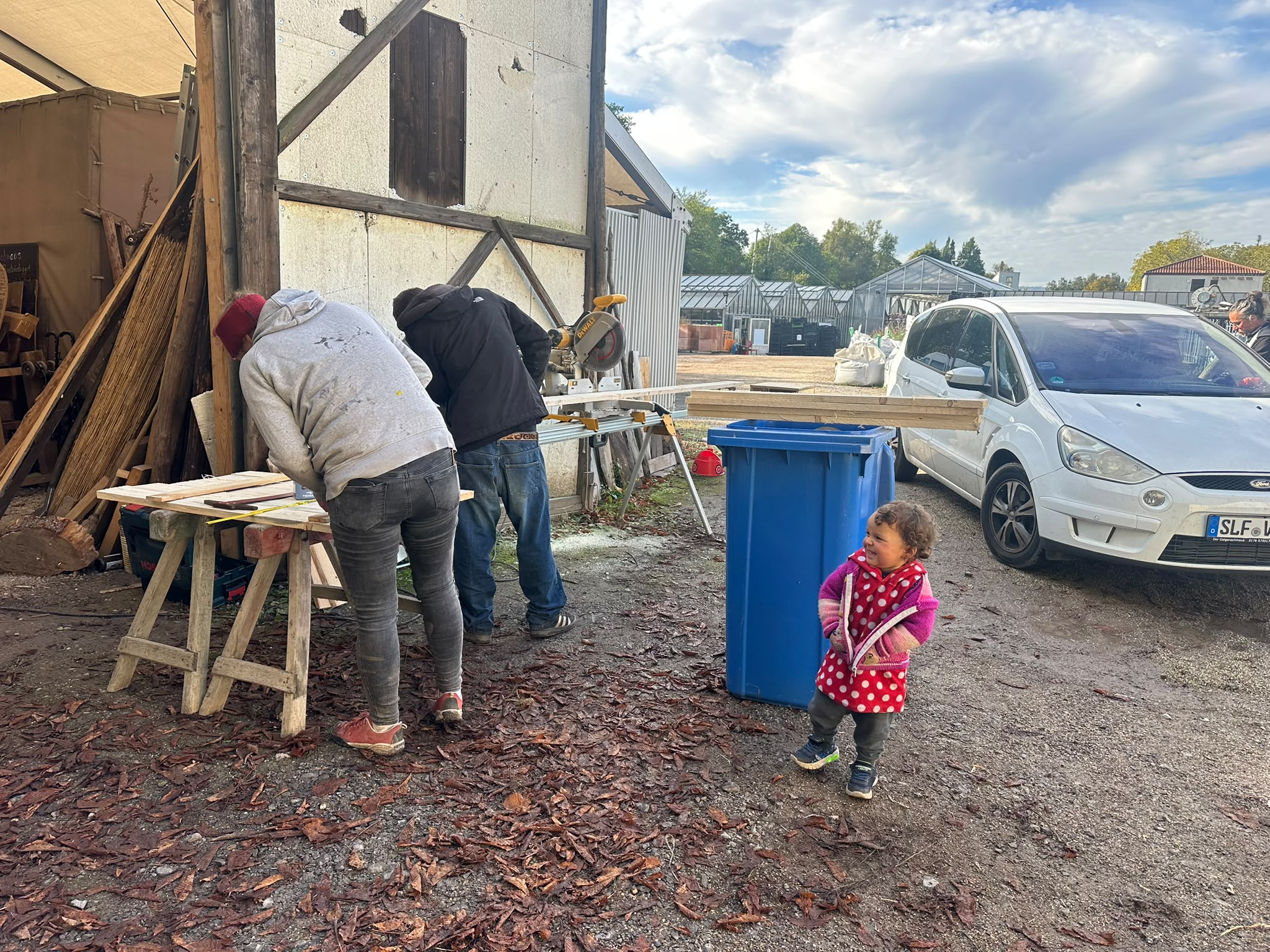 Zwei Helfer bearbeiten Holz im Werkstattbereich, ein Kind schaut zu